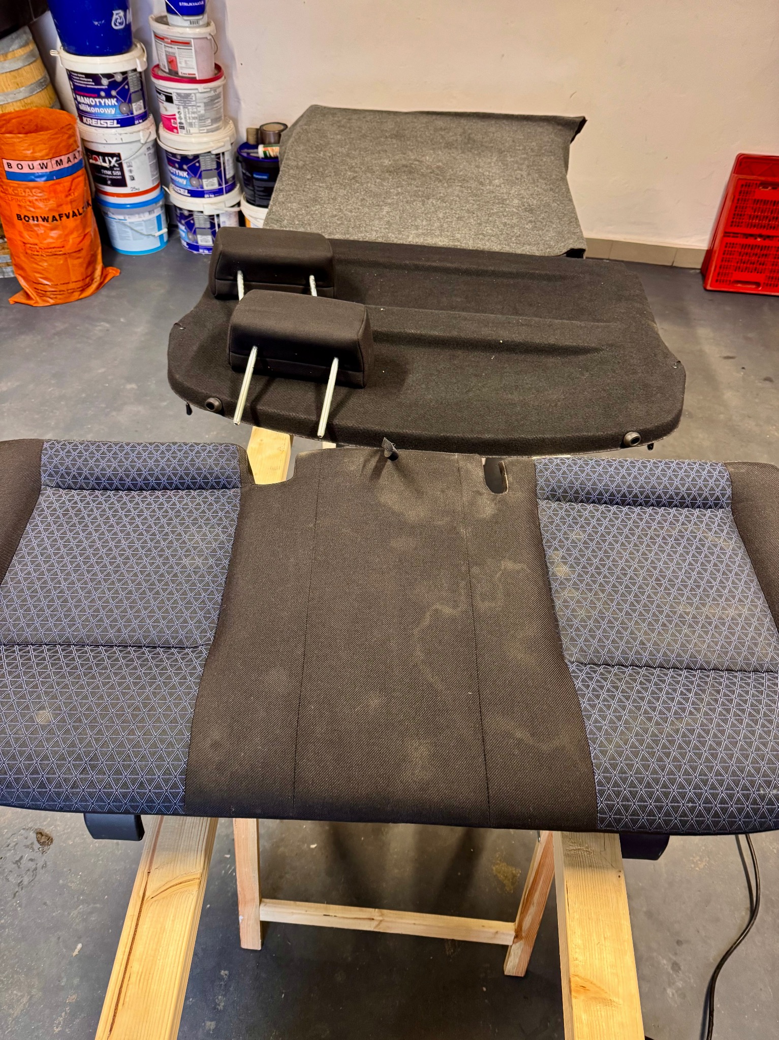 Tapicerka samochodowa z wyraźnym wzorem, rozłożona na drewnianym stojaku, gotowa do czyszczenia. W tle widoczne akcesoria i chemia do czyszczenia.