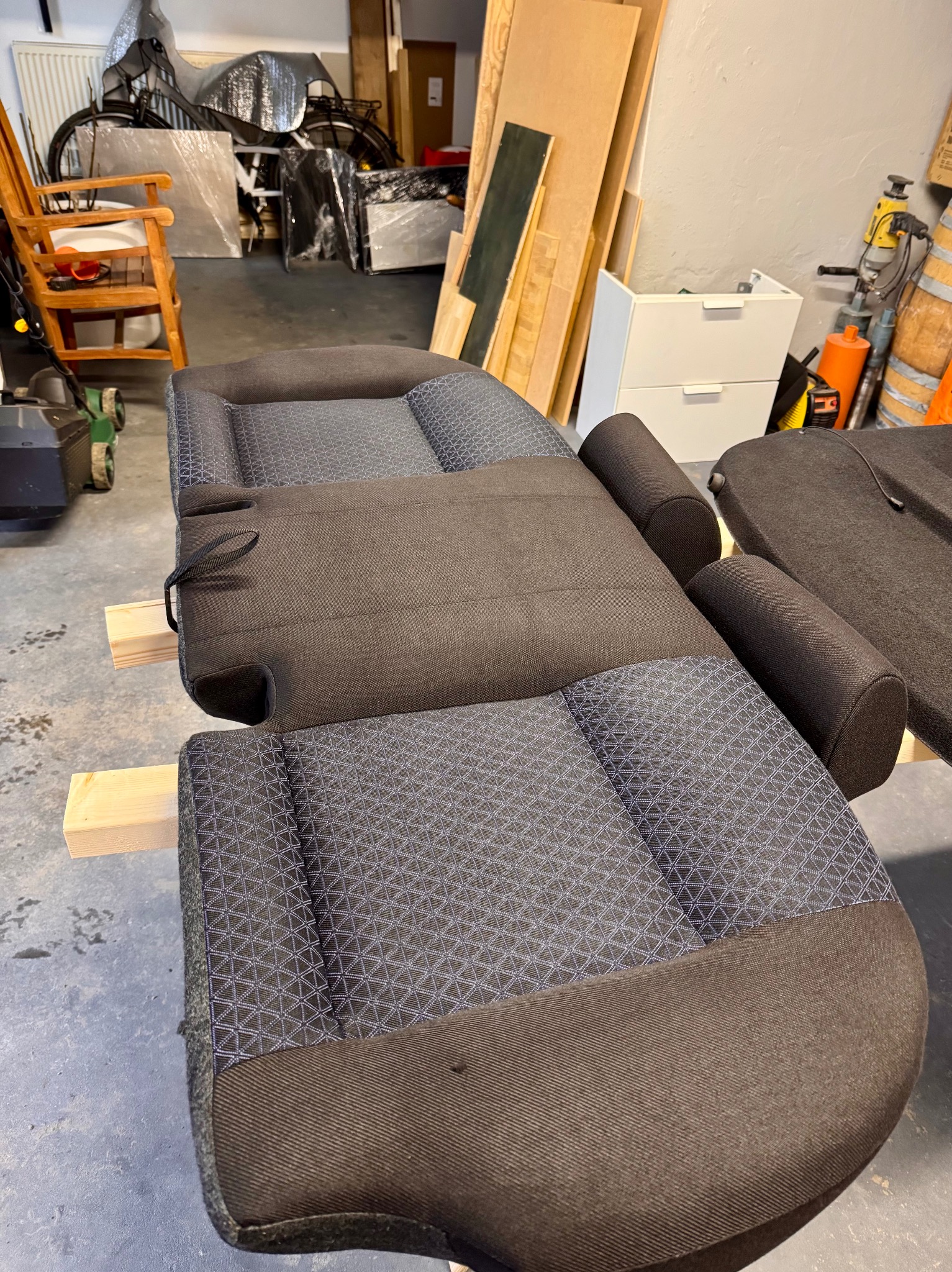 Tapicerka samochodowa z geometrycznym wzorem, rozłożona na drewnianych belkach w warsztacie. Widoczne detale szwów i faktury materiału. Przygotowana do prania lub renowacji.