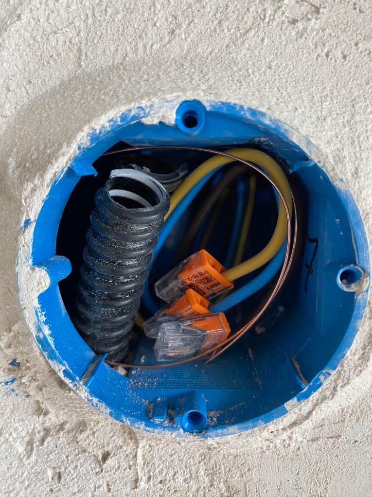 Niebieska puszka instalacyjna w ścianie z przewodami (żółty, niebieski, miedziany) i złączkami WAGO. Widoczna karbowana rurka. Ściana w surowym tynku.