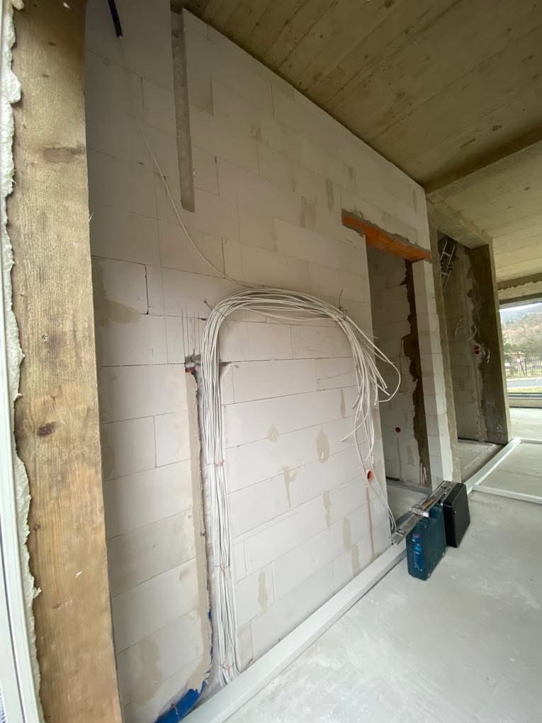 Ściana z betonu komórkowego w trakcie prac instalacyjnych. Widoczne przewody elektryczne ułożone w pętlę, przygotowane do rozprowadzenia w bruzdach. W tle surowy betonowy strop.