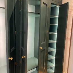 Elegancka, ciemnozielona szafa wnękowa z oświetleniem wewnętrznym i złotymi uchwytami, wykonana na wymiar w Bielsko-Białej. Otwarte drzwi ukazują półki.