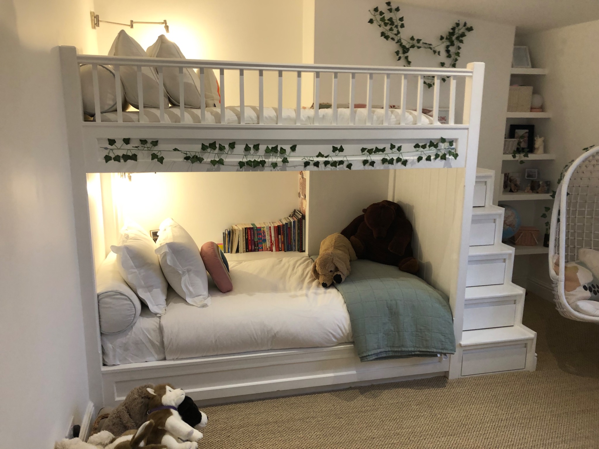 Białe łóżko piętrowe z drabinką i dekoracjami roślinnymi w pokoju dziecięcym w Bielsko-Białej. Na dolnym poziomie pluszaki i książki.