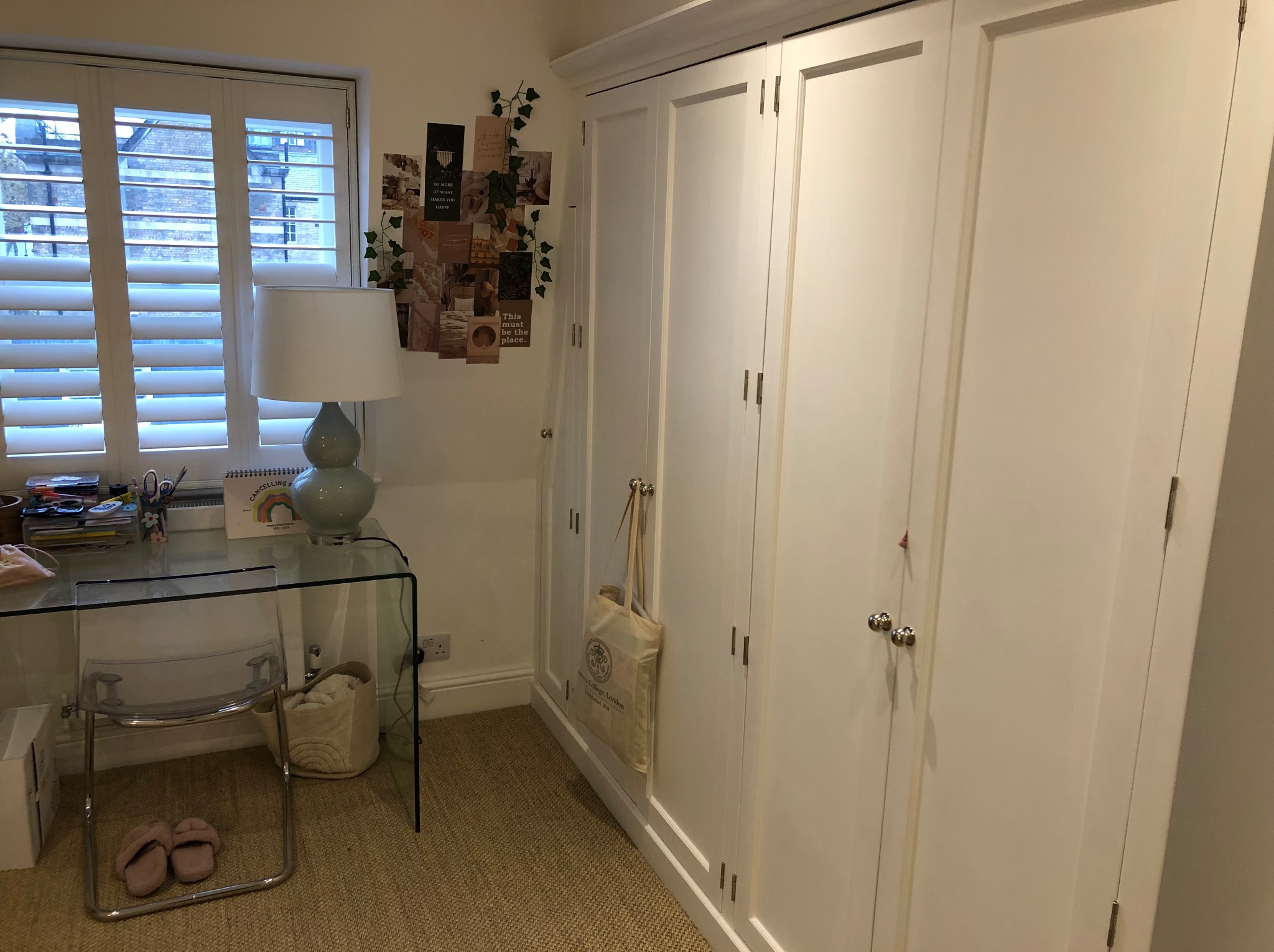 Biała szafa wnękowa z trzema drzwiami, widoczna z perspektywy pokoju z biurkiem i żaluzjami. Na szafie dekoracje i torba. Jasne wnętrze.