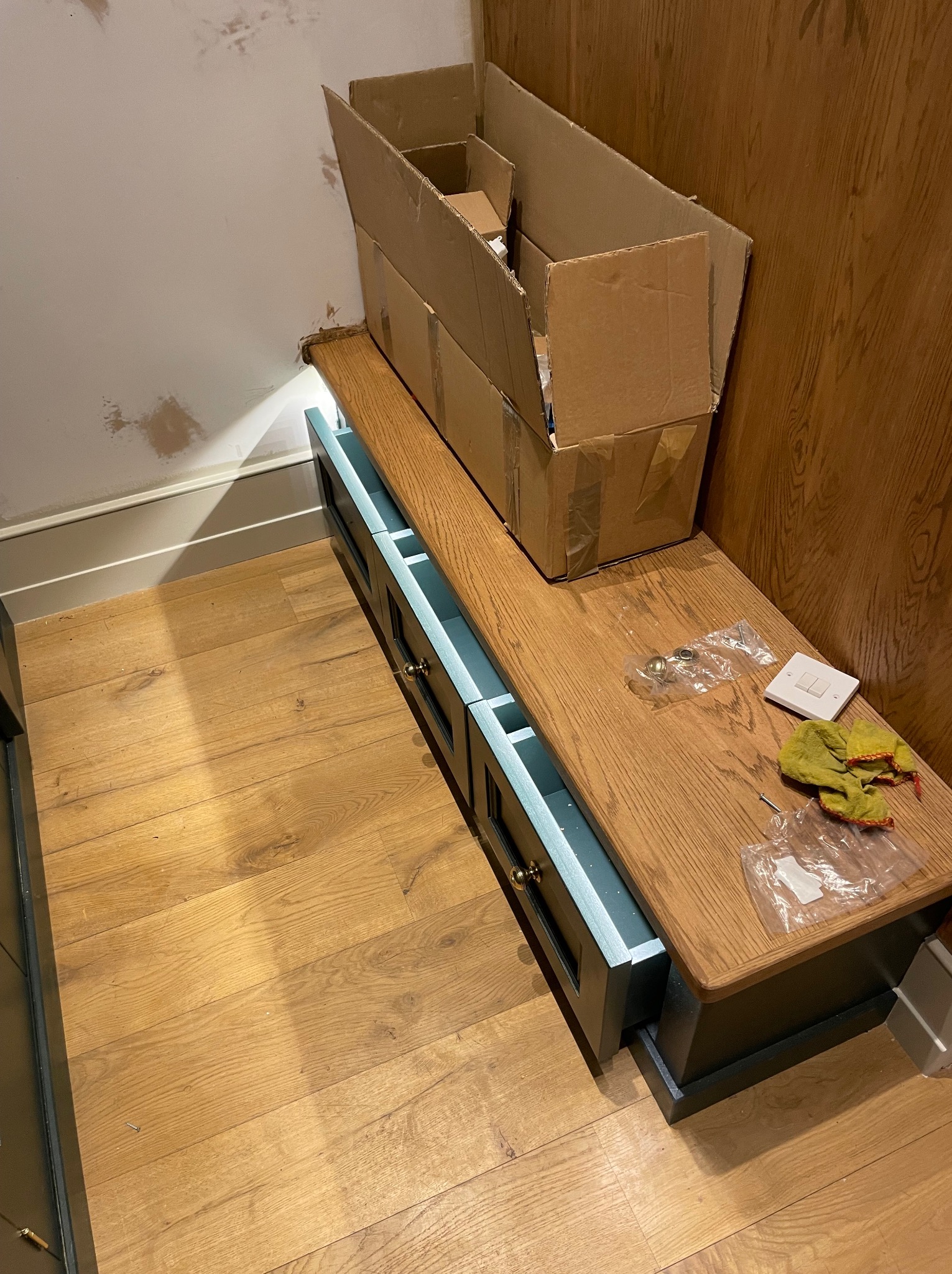 Montaż szafki z szufladami wnękowej z drewnianym blatem. Widoczne akcesoria montażowe, karton i fragment ściany z niedokończonymi pracami wykończeniowymi.