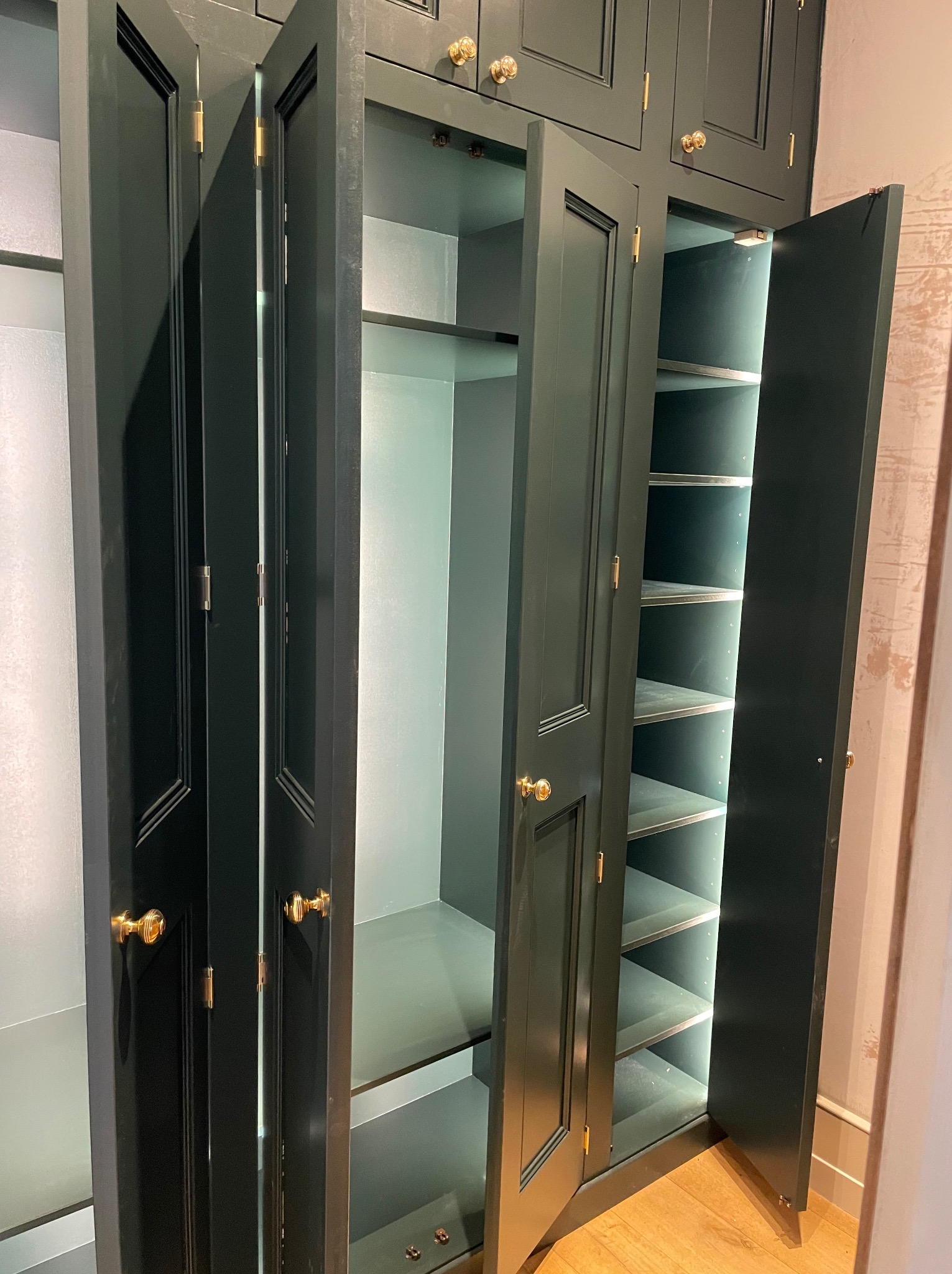 Elegancka, ciemnozielona szafa wnękowa z oświetleniem wewnętrznym i złotymi uchwytami, wykonana na wymiar w Bielsko-Białej. Otwarte drzwi ukazują półki.