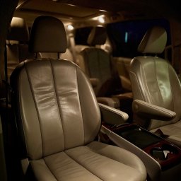 TOKO BOOS - Wnętrze luksusowego busa z beżowymi skórzanymi fotelami, oświetlone ciepłym światłem, sugerujące komfortową podróż. Widoczne detale wykończenia z elementami drewna.