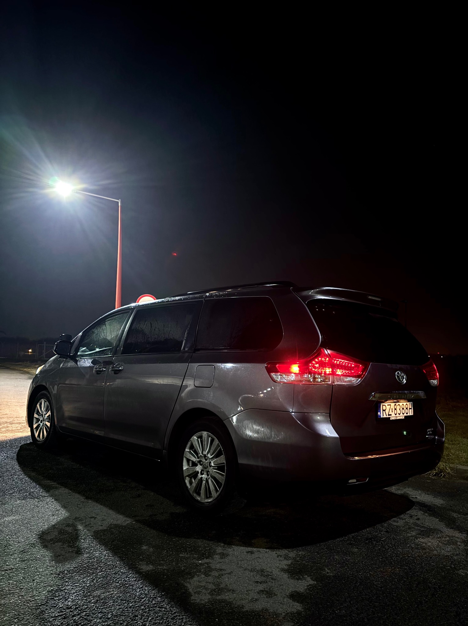 Szary minivan Toyota Sienna, widziany z tyłu w nocy pod latarnią. Widoczne mokre ślady na karoserii i asfalcie. Tablica rejestracyjna RZ 8388H.