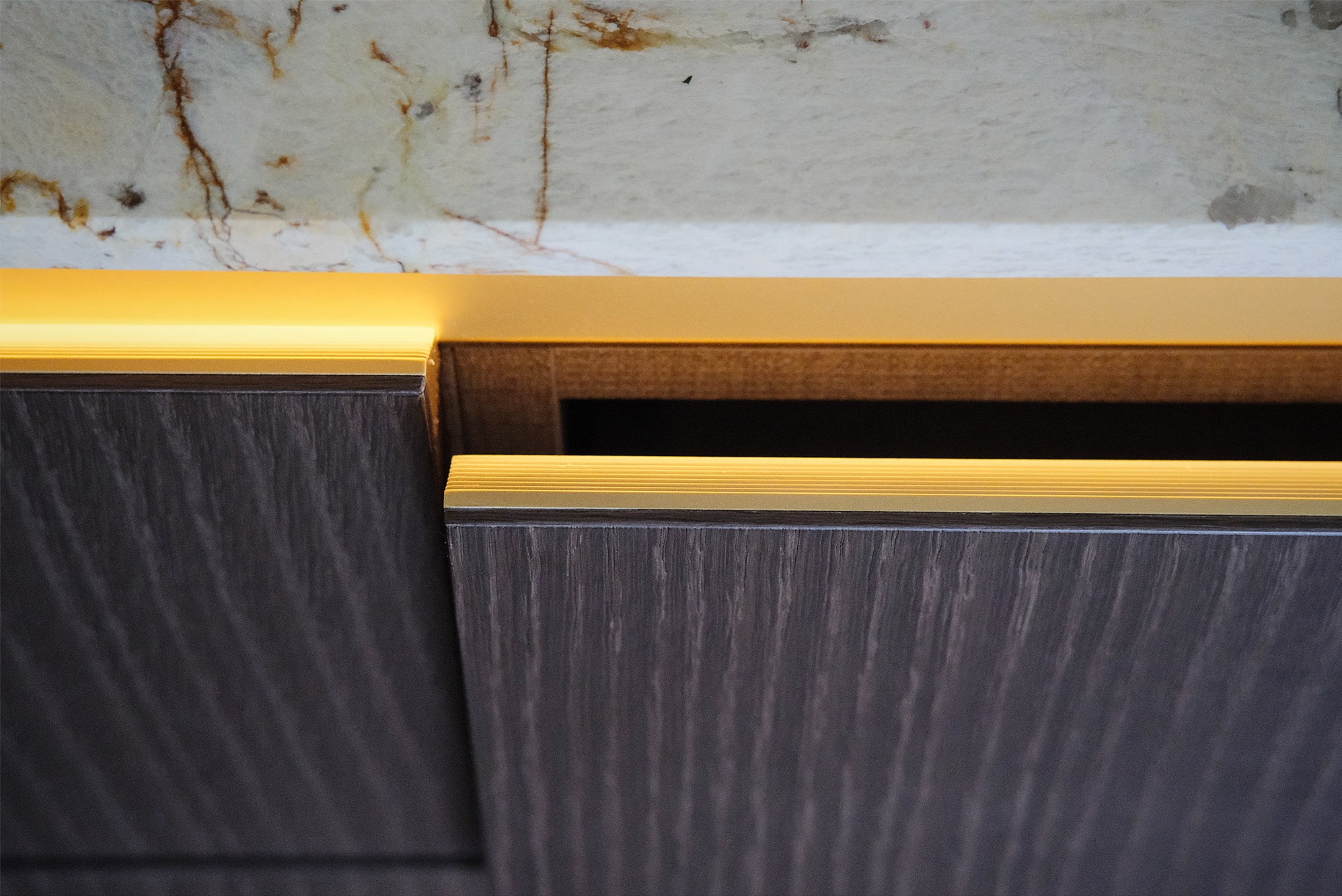 Detal zabudowy meblowej z podświetleniem LED, widoczny fragment blatu z marmurowym wzorem. Ujęcie z bliska, podkreślające precyzję wykonania i nowoczesny design.