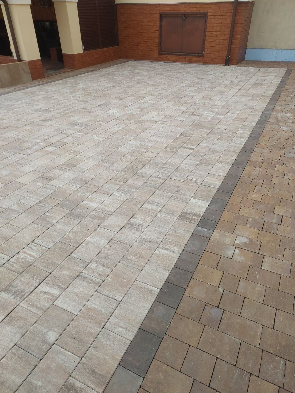 Ułożona kostka brukowa w odcieniach beżu i brązu, tworząca wzór na podjeździe. Widoczne detale łączeń i faktury kostki, z obramowaniem z ciemniejszych elementów.