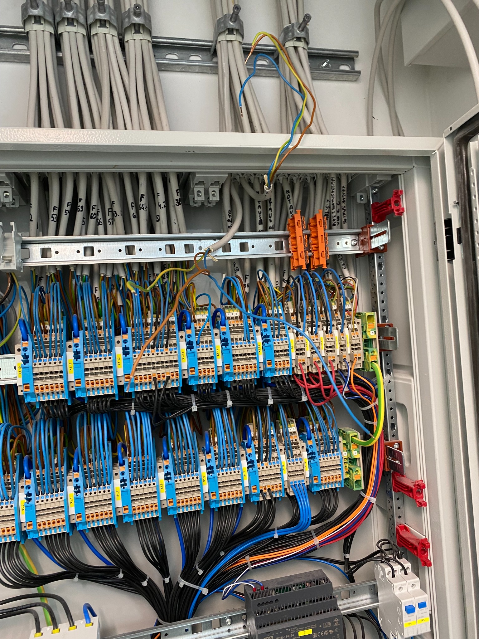 Rozdzielnica elektryczna z precyzyjnie ułożonymi przewodami oznaczonymi numerami, widoczne bezpieczniki i listwy zaciskowe wewnątrz metalowej obudowy.