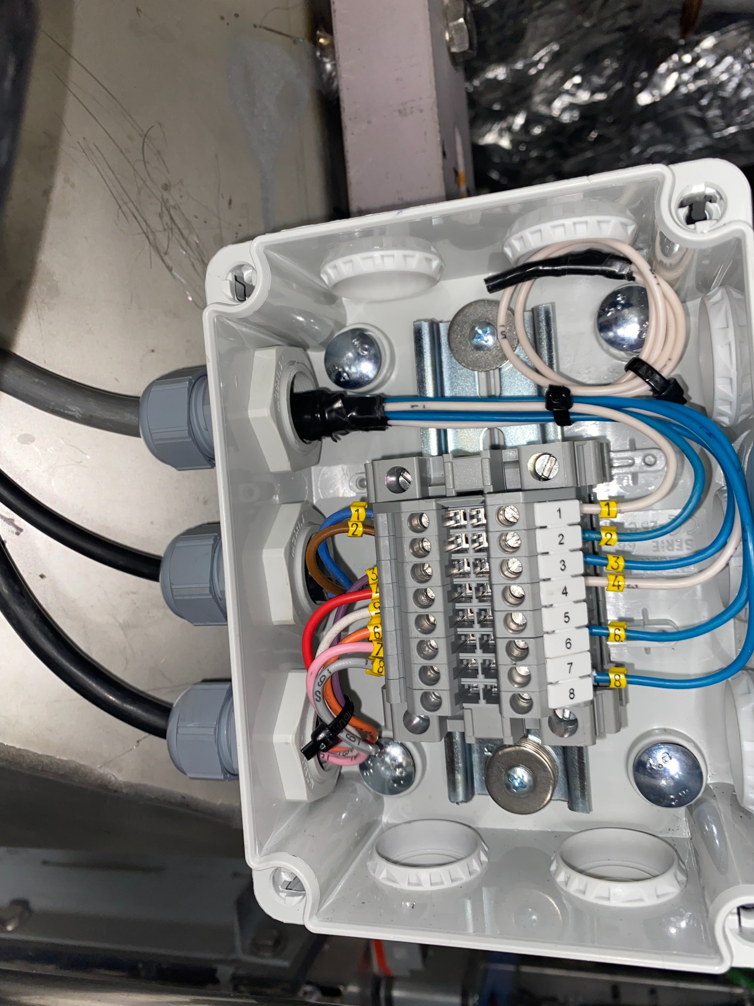 Rozdzielnica elektryczna z podłączonymi przewodami wewnątrz białej obudowy. Widoczne złącza, kable w różnych kolorach i oznaczenia numerów.