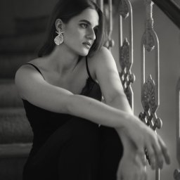 Marcin Pycha Studio - Portret kobiety w czerni, siedzącej na schodach z ozdobną balustradą. Zdjęcie w odcieniach szarości, z delikatnym oświetleniem podkreślającym detale biżuterii.