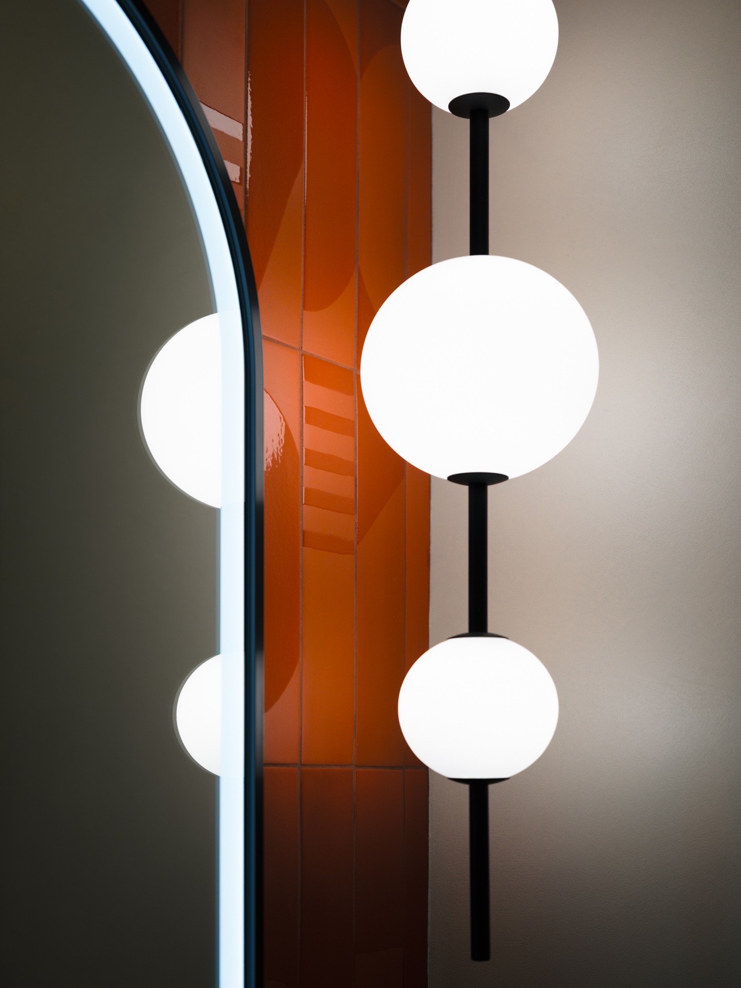Minimalistyczne wnętrze: lampa kulista na czarnym stelażu, pomarańczowe płytki i lustro z podświetleniem LED tworzą nowoczesny, geometryczny design.