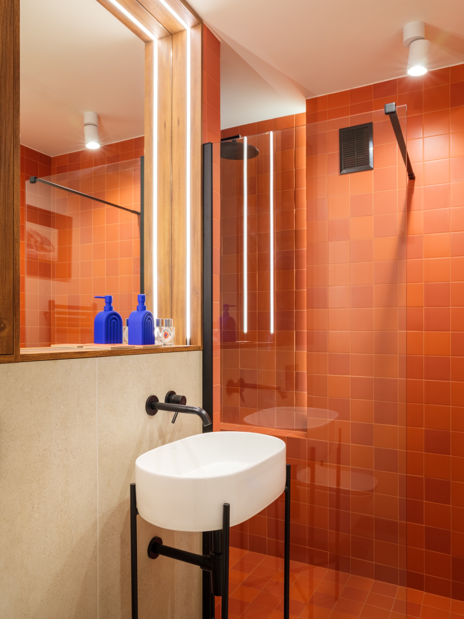 Pomarańczowa łazienka z kabiną prysznicową typu walk-in, białą umywalką na czarnym stelażu i akcentami w kolorze kobaltowym. Nowoczesny design z podświetleniem LED.