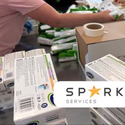 SPARK SERVICES SPÓŁKA Z OGRANICZONĄ ODPOWIEDZIALNOŚCIĄ - Pakowanie torebek śniadaniowych z suwakiem w kartony. Widoczne opakowania jednostkowe i rolka taśmy klejącej. Praca wykonywana w rękawicach ochronnych.