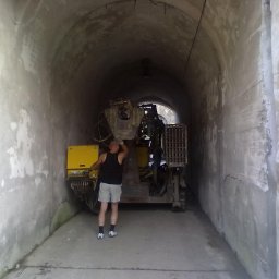 Firma Handlowo-Usługowa Piotr Czyszczoń - Wnętrze tunelu z maszyną wiertniczą i mężczyzną w podkoszulku, prawdopodobnie podczas prac geologicznych lub wiertniczych. Szare, betonowe ściany tunelu.