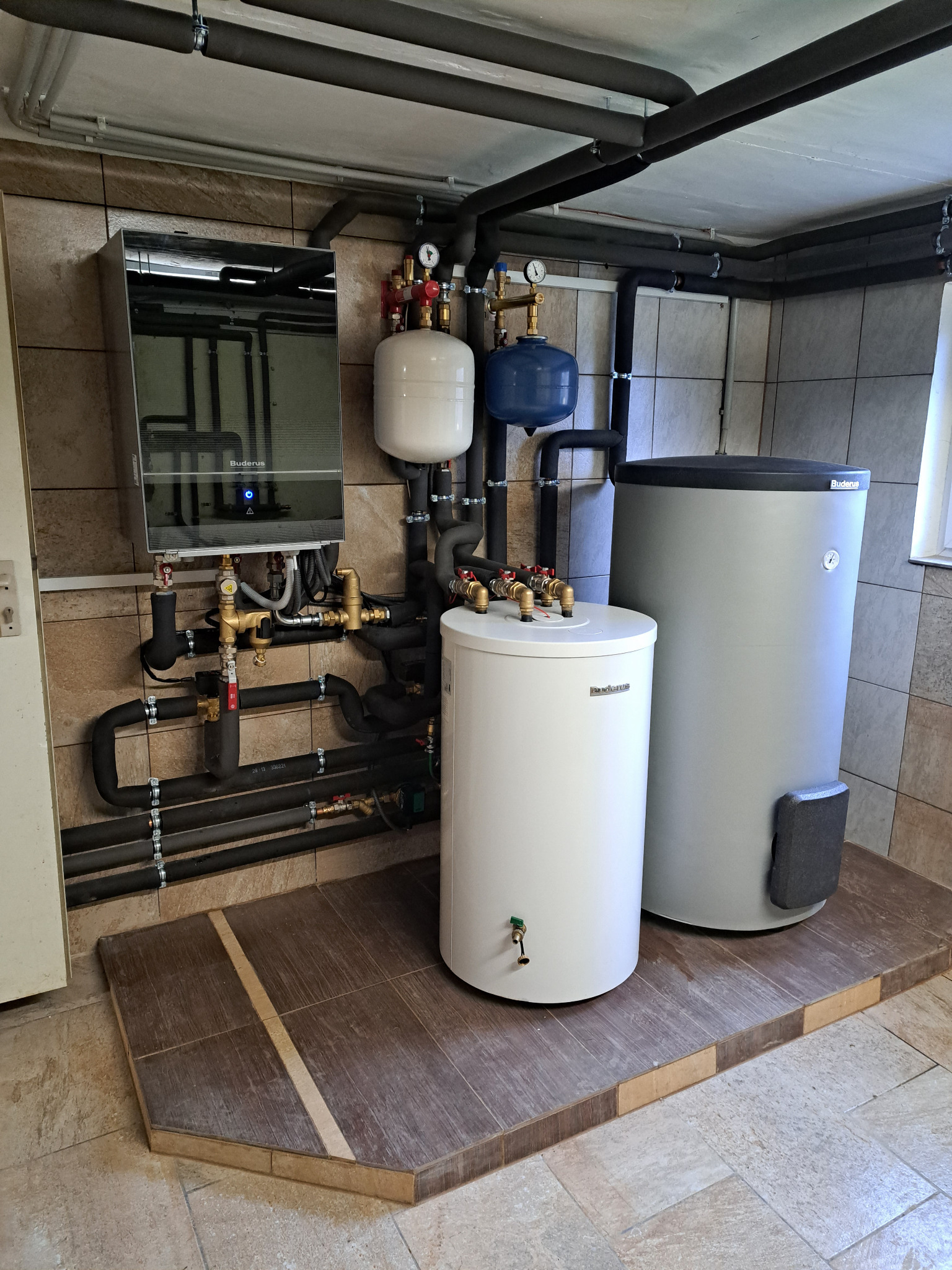Kompletna instalacja grzewcza Buderus z zbiornikami i modułem sterującym, zamontowana w pomieszczeniu z wykończeniem z płytek ceramicznych.