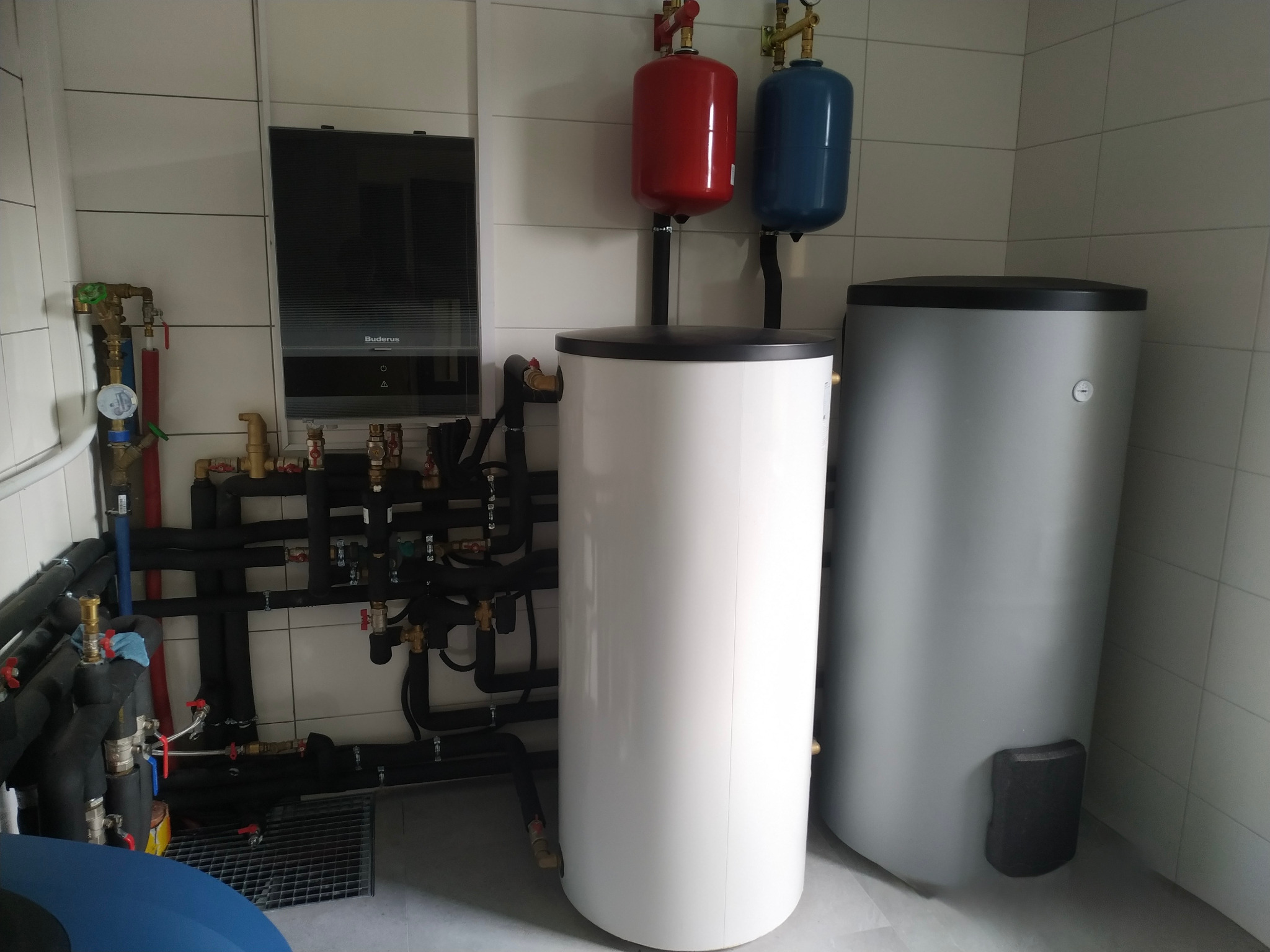 Instalacja Buderus Bosch monoblok z zbiornikami buforowymi w kotłowni z białymi płytkami. Widoczne rury, zawory i elementy montażowe.