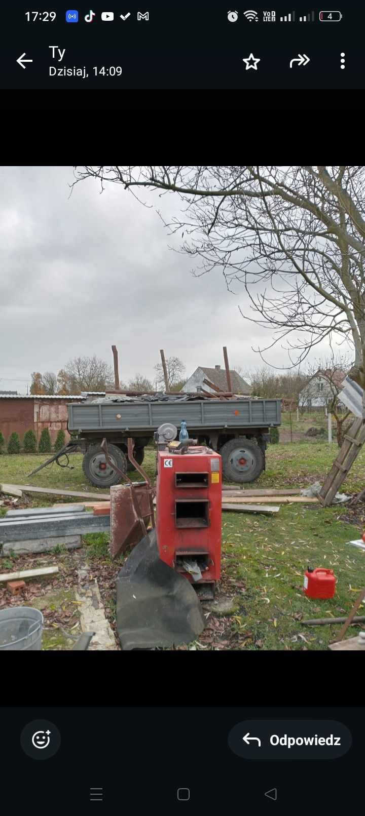 Przyczepa z elementami po rozbiórce, na pierwszym planie piec. Widoczne pozostałości po pracach rozbiórkowych na zewnątrz budynku. Niebo pochmurne.