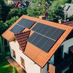 STAN ENERGIA POLSKA PROSTA SPÓŁKA AKCYJNA - Dom jednorodzinny z panelami fotowoltaicznymi na dachu z czerwonej dachówki, widok z góry, antena satelitarna na kominie, zielone otoczenie.