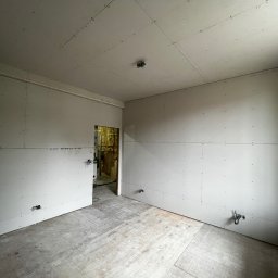 Krzysztof Sowinski - Pokój w trakcie remontu: ściany i sufit wyłożone płytami kartonowo-gipsowymi, widoczne łączenia i wkręty. Podłoga wyłożona płytami OSB. Otwór drzwiowy z widoczną izolacją.