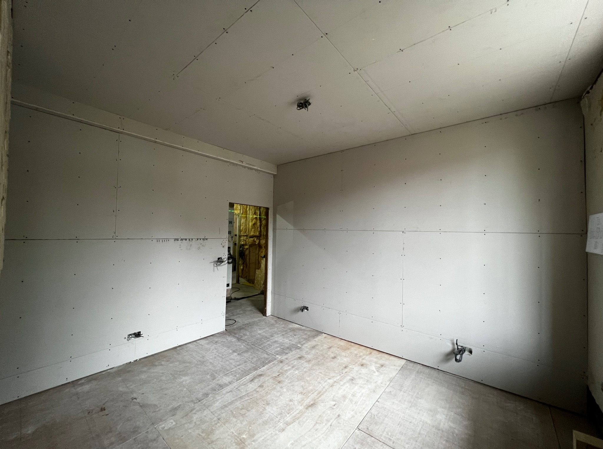Pokój w trakcie remontu: ściany i sufit wyłożone płytami kartonowo-gipsowymi, widoczne łączenia i wkręty. Podłoga wyłożona płytami OSB. Otwór drzwiowy z widoczną izolacją.