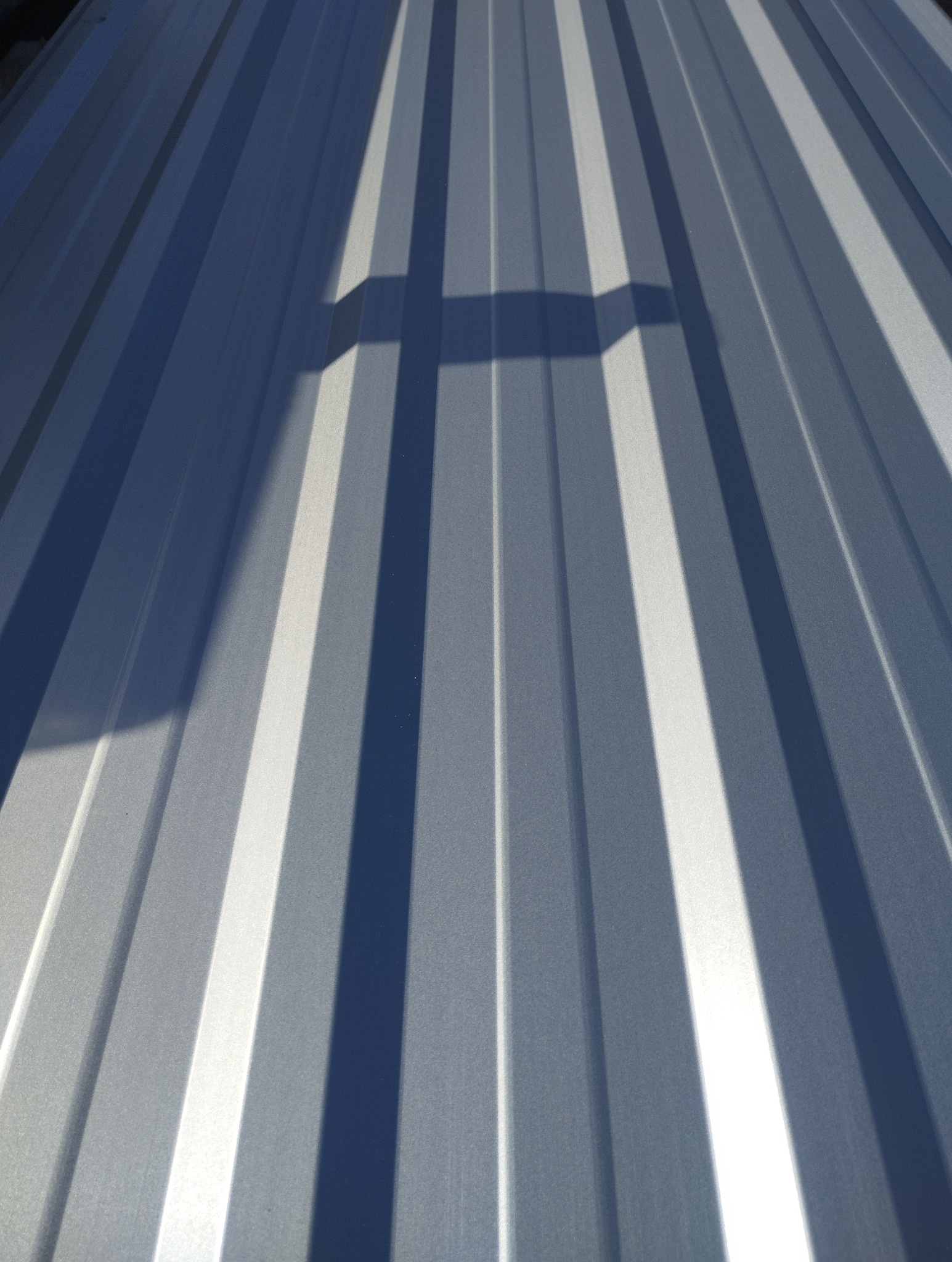 Szara blacha trapezowa z wyraźnym cieniem, ukazująca regularny wzór i fakturę materiału. Ujęcie z bliska, podkreślające detale i geometrię profilu.