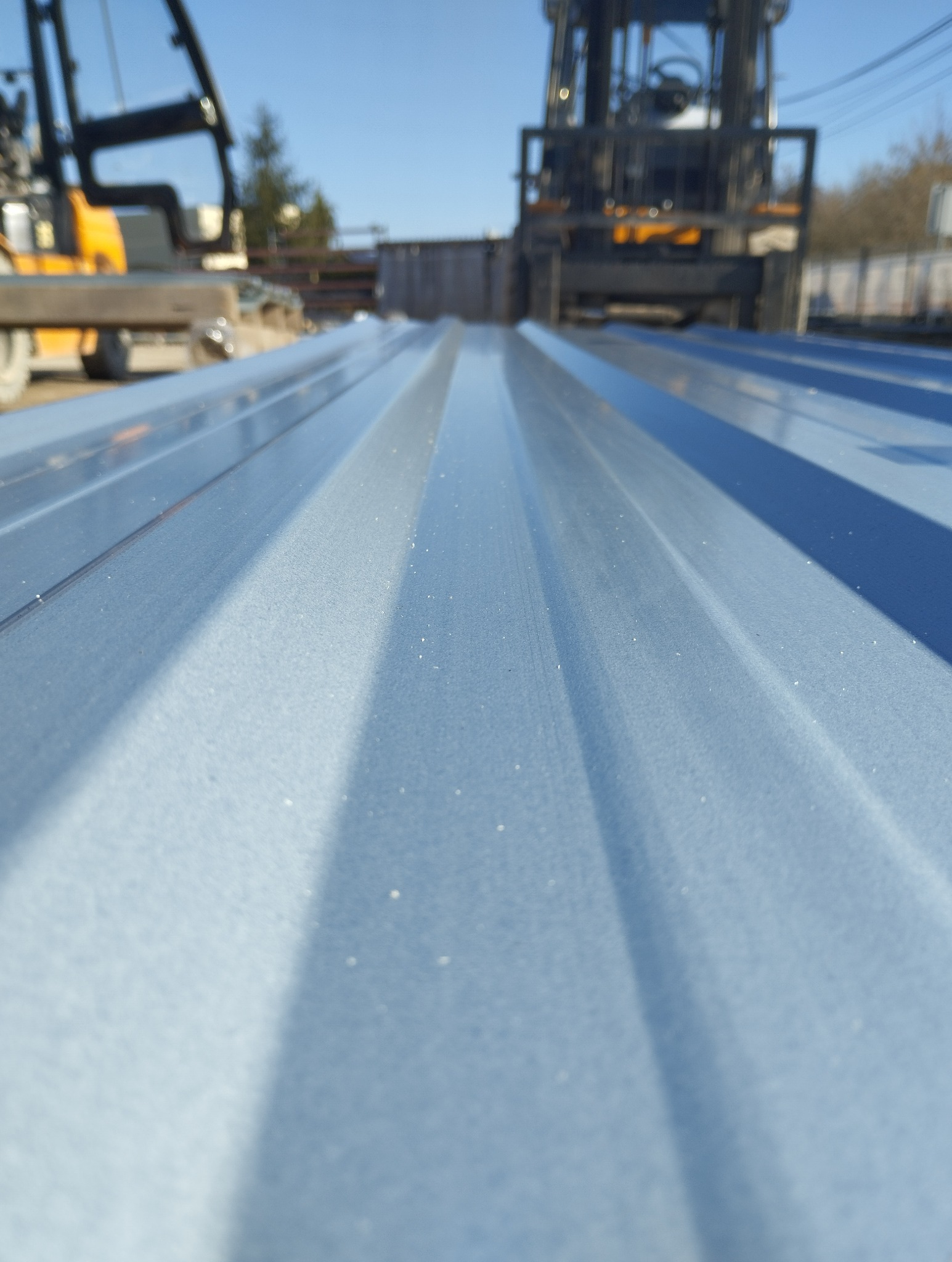 Błękitna, trapezowa powierzchnia z widocznymi w tle wózkami widłowymi. Ujęcie z niskiej perspektywy podkreśla fakturę materiału i jego regularny wzór.