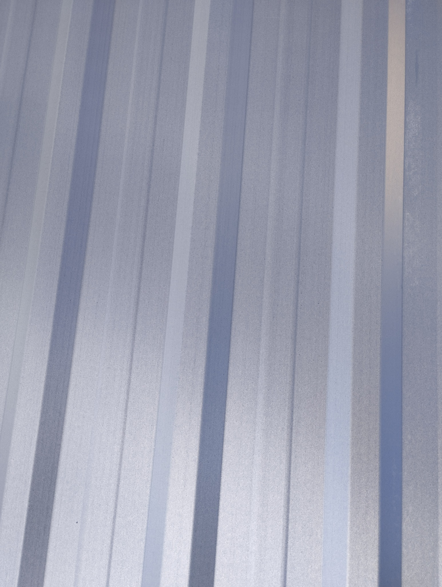 Szara blacha trapezowa w zbliżeniu, widoczne pionowe przetłoczenia i delikatna faktura materiału. Oświetlenie tworzy subtelne cienie.