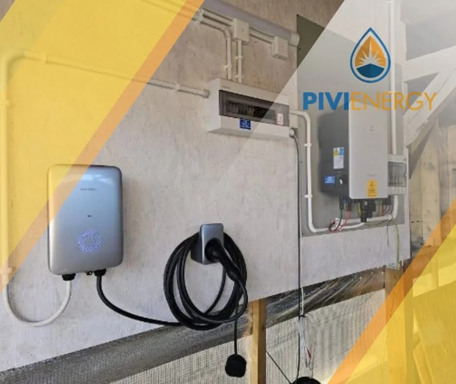 Szary magazyn energii na ścianie obok rozdzielnicy i inwertera. Kabel z wtyczką zwinięty na uchwycie. Elementy instalacji wewnątrz budynku.