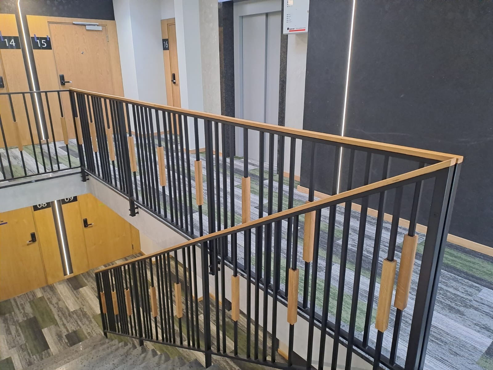 Nowoczesna balustrada schodowa z czarnymi pionowymi prętami i drewnianymi akcentami, widok z góry na klatkę schodową w budynku mieszkalnym.