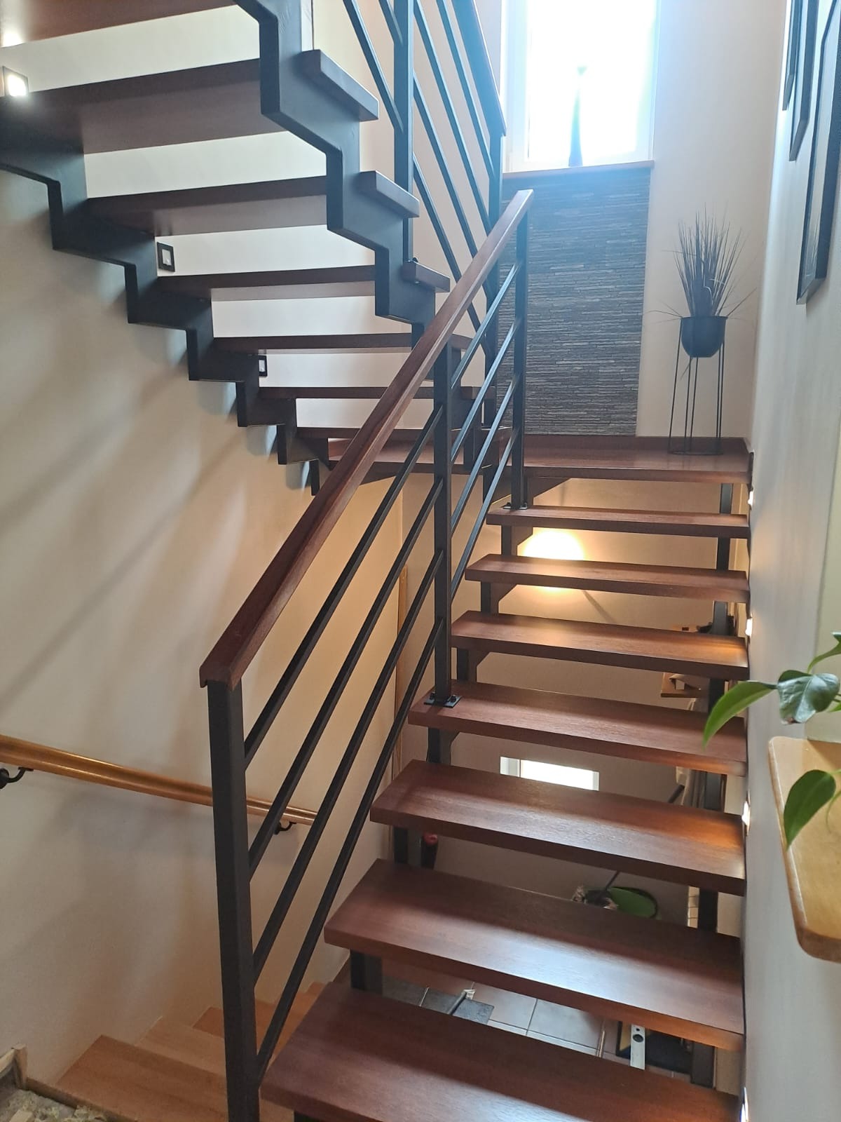 Nowoczesne schody drewniane z czarną metalową balustradą i drewnianą poręczą. Stopnie podświetlone punktowo, widok z dołu. Minimalistyczny design.