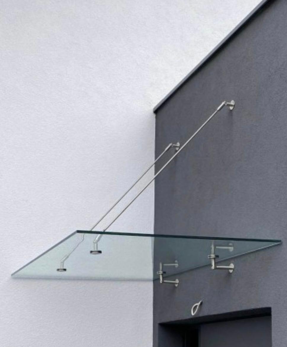 Szklany daszek nad wejściem, wsparty na metalowych linkach i uchwytach, minimalistyczny design, szara ściana budynku.