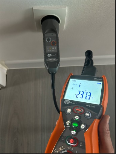 Pomiar napięcia w gniazdku sufitowym za pomocą miernika Sonel MPI-507. Wyświetlacz pokazuje 237.3V. Widoczny kabel i wtyczka miernika WS-03.