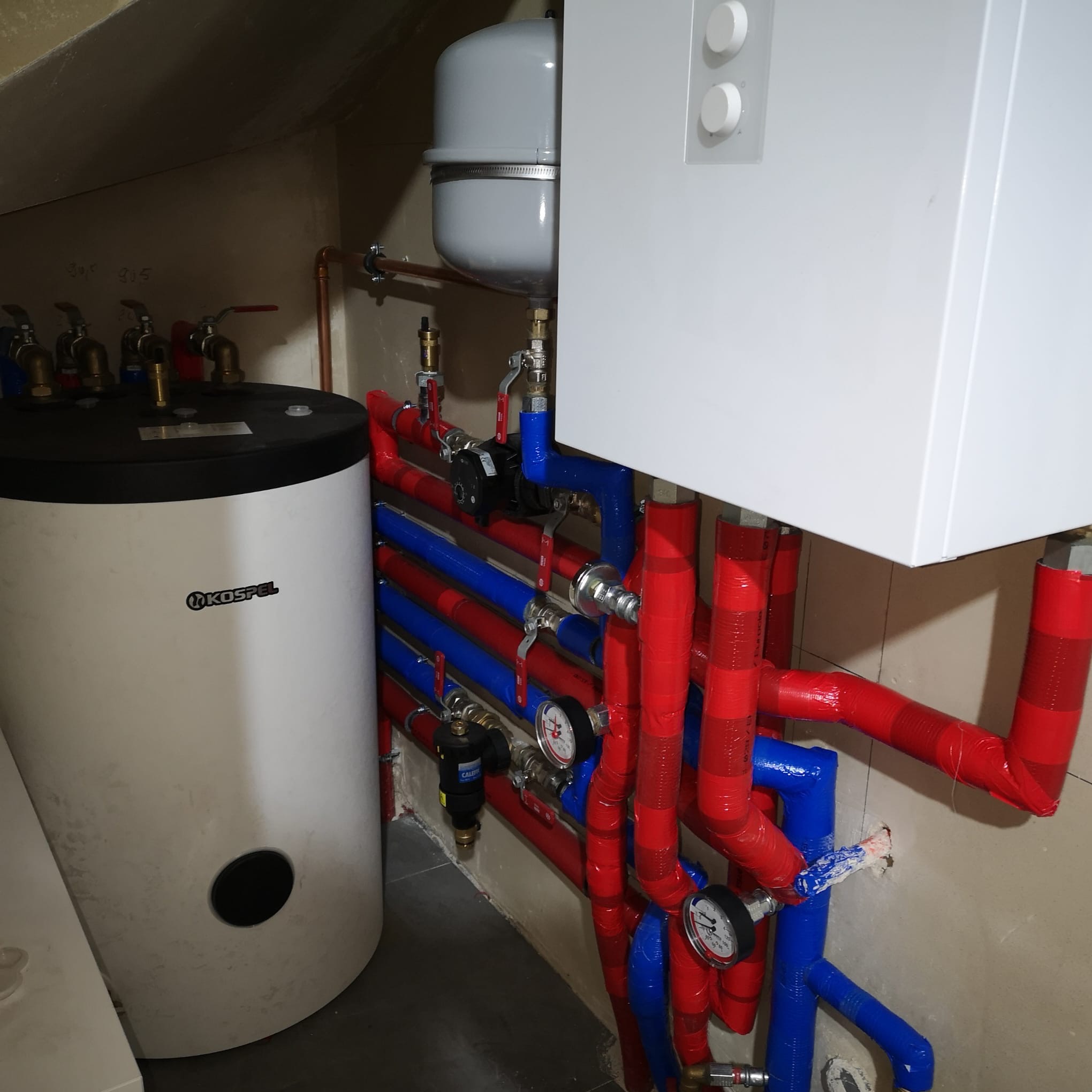Biały piec gazowy i instalacja CO z rurami w izolacji czerwono-niebieskiej w kotłowni w Gdańsku. Widoczne manometry i zawory. Kospel.