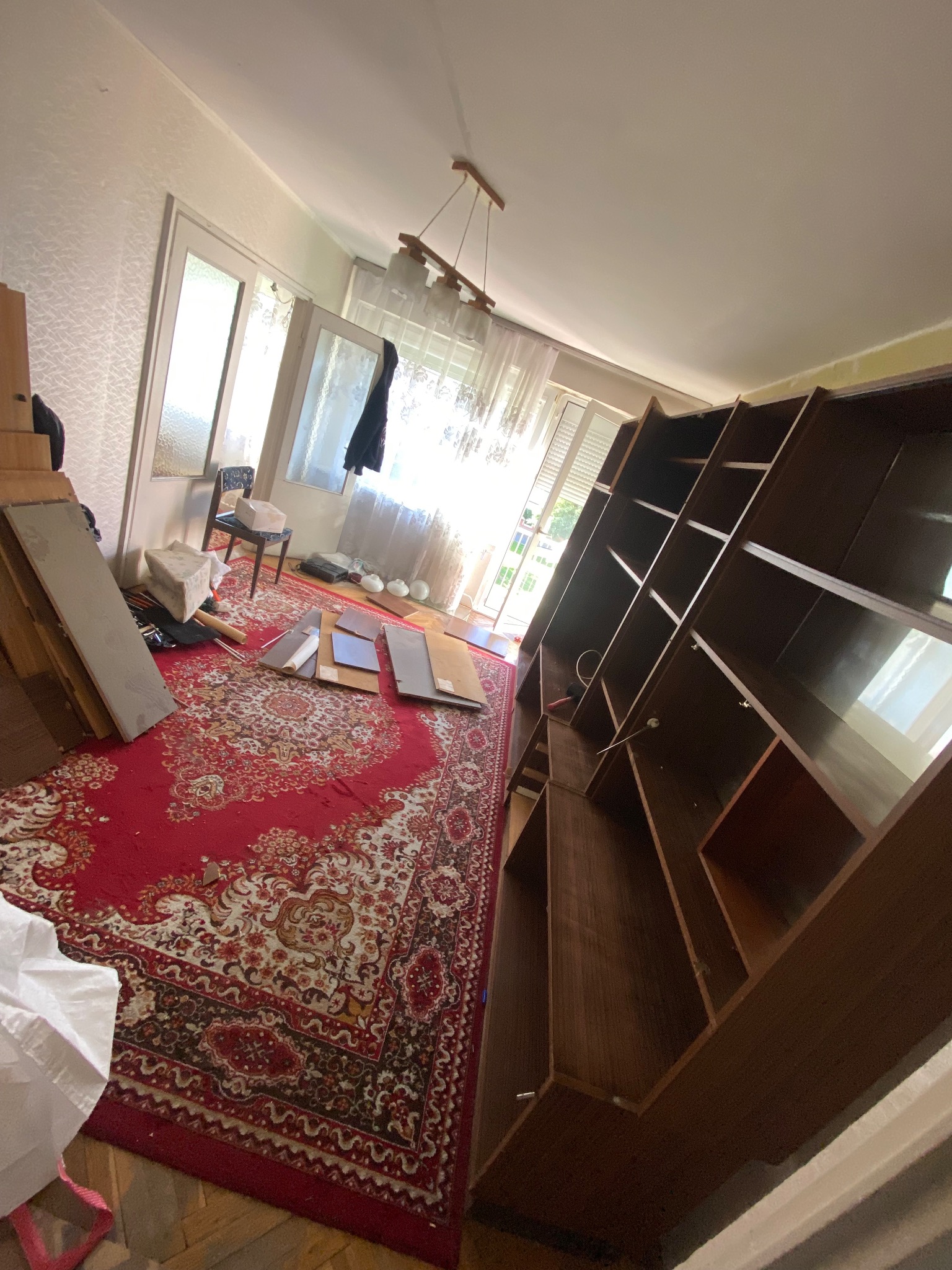 Pokój w trakcie opróżniania: rozłożony regał, elementy wyposażenia na czerwonym dywanie, widoczne ślady po demontażu. Przygotowanie do sprzątania.