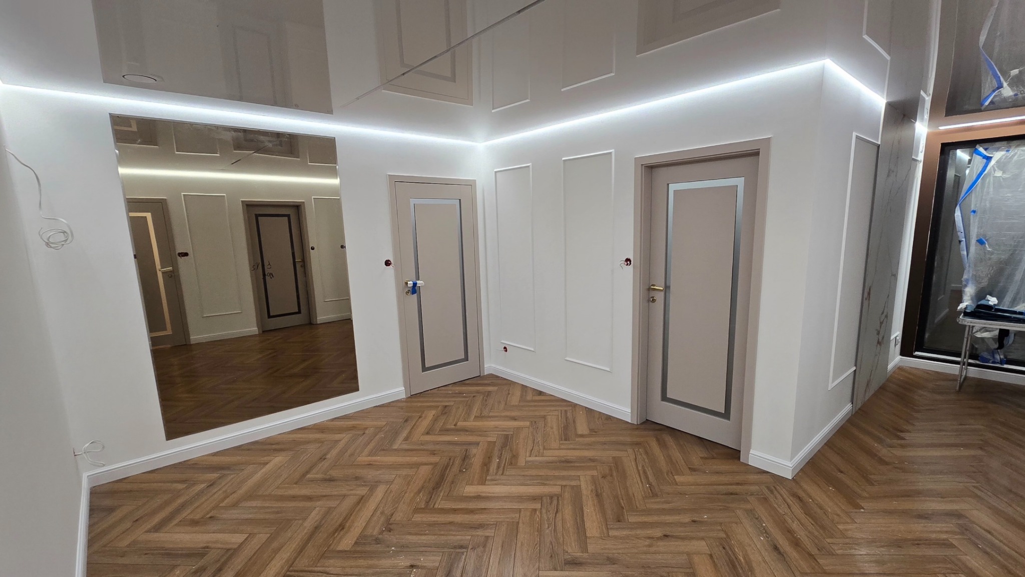 Wykończone wnętrze: parkiet w jodełkę, białe ściany z dekoracyjnymi listwami, drzwi z szarymi obramowaniami, lustro i podwieszany sufit z oświetleniem LED.