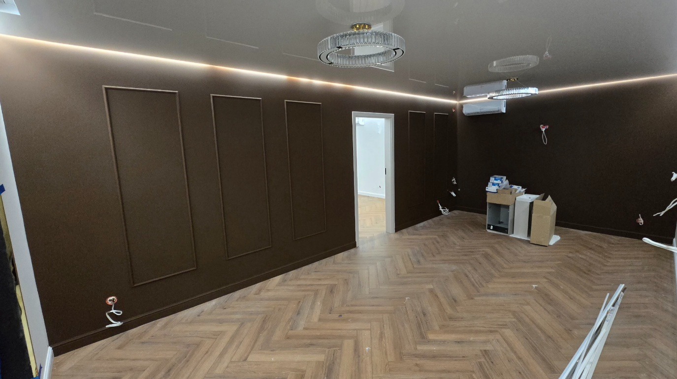 Eleganckie wykończenie wnętrza: brązowe ściany z panelami, parkiet w jodełkę, nowoczesne oświetlenie LED i designerski żyrandol. Widoczne elementy instalacji elektrycznej.