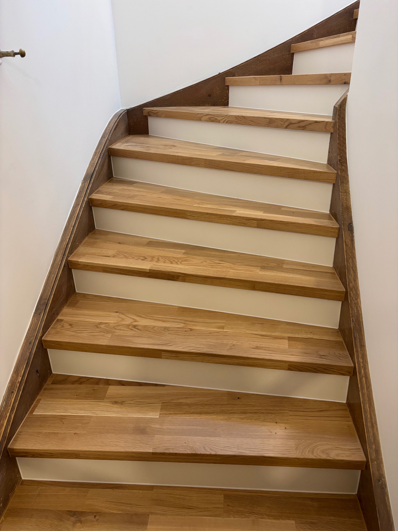 Drewniane schody z jasnymi podstopnicami, widok z dołu. Naturalne wykończenie drewna, zakrzywiony bieg schodów, minimalistyczny design.