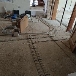 Serhii Rakomin - Rozprowadzone kable elektryczne w szarych rurkach na surowej podłodze w trakcie remontu domu. Widoczne skrzynki, narzędzia i schody w tle. Instalacja elektryczna przed tynkowaniem.