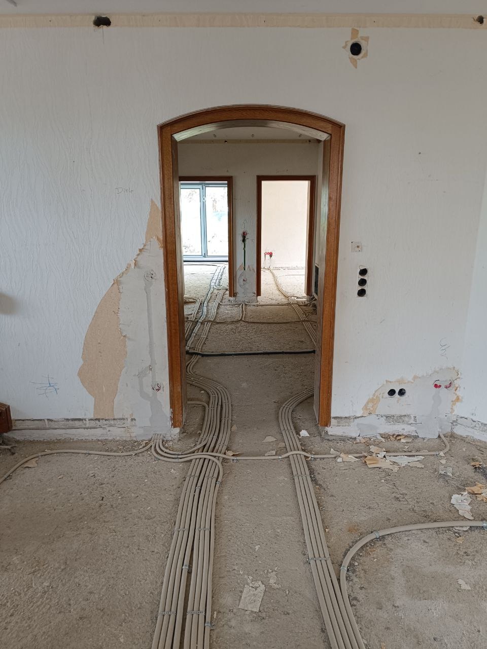 Rozprowadzone kable elektryczne w peszlach na podłodze w trakcie remontu mieszkania. Widoczne ślady po kuciu w ścianach i otwory na gniazdka.