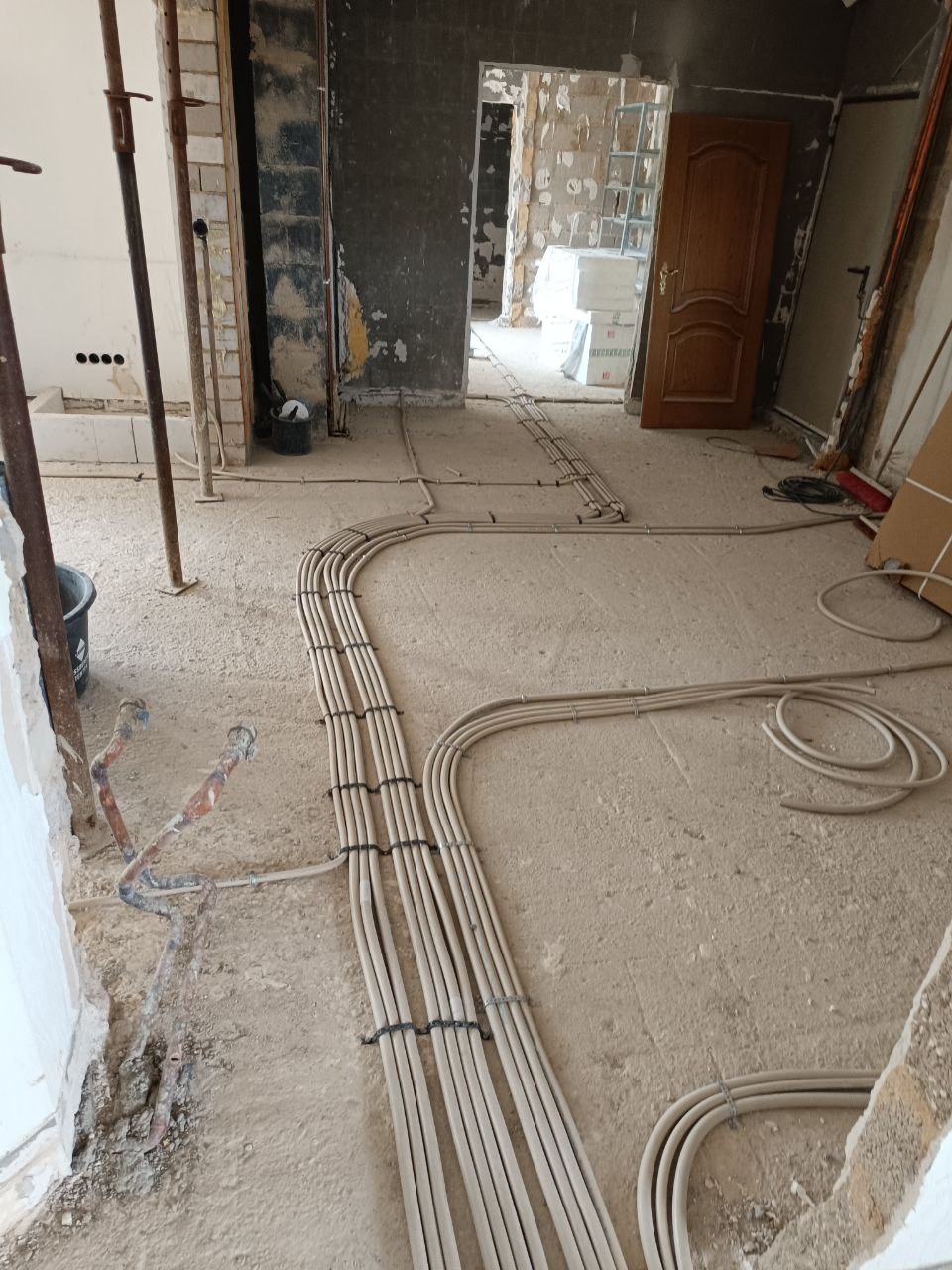 Układanie kabli elektrycznych w nowym budynku w Sosnowcu. Kable prowadzone po podłodze, zabezpieczone opaskami. Widoczne surowe ściany i elementy konstrukcyjne.