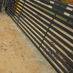 Arkadiusz Nowakowski Usługi Spawalnicze - Nowoczesna, pozioma brama wjazdowa z szarych, metalowych profili na tle domu jednorodzinnego i jesiennego krajobrazu. Widoczne narzędzia i elementy montażowe.