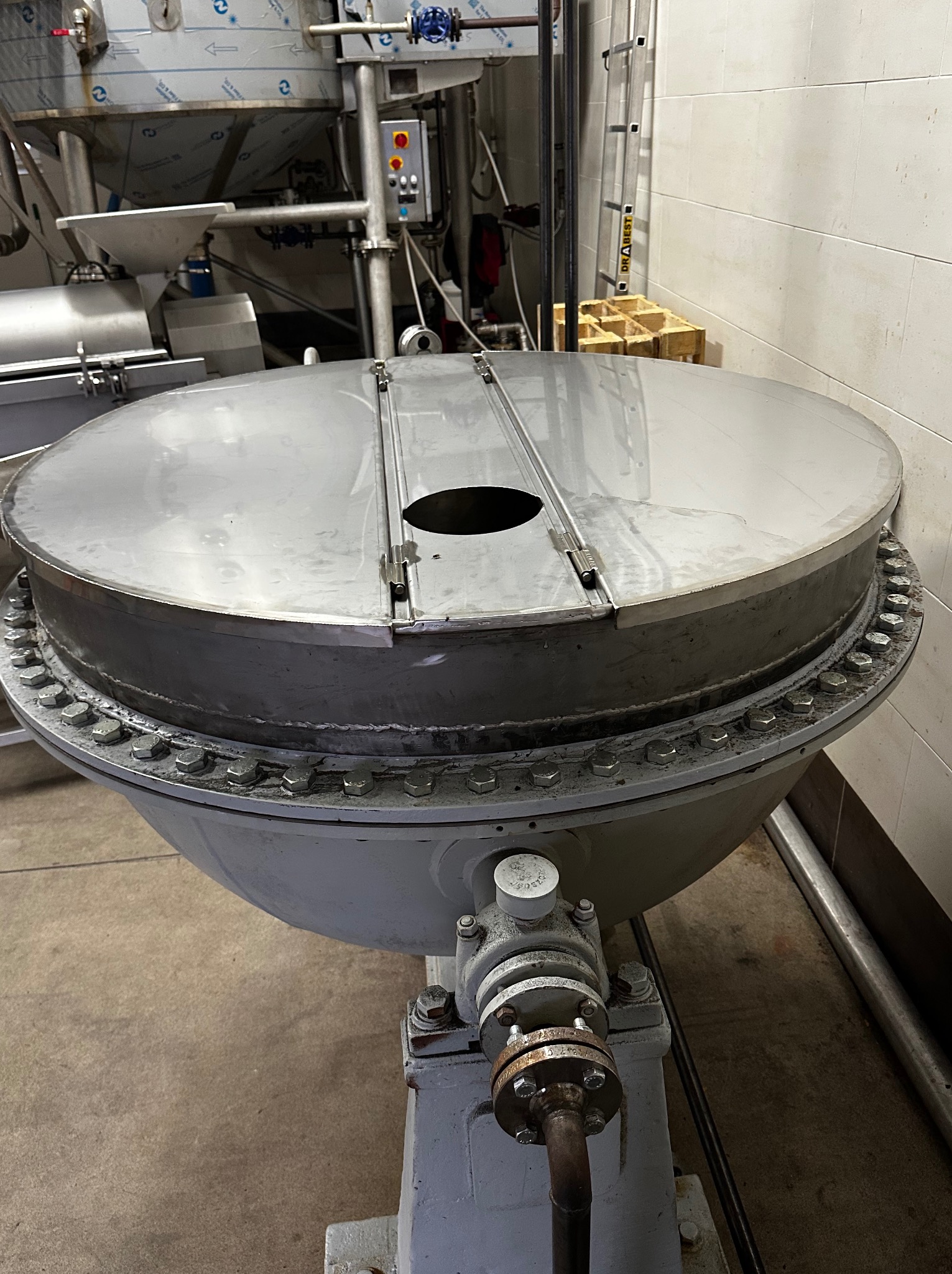 Metalowa konstrukcja przemysłowa z okrągłą pokrywą, mocowana na śruby, z widocznymi elementami instalacji i rur. Szara podstawa i stalowa góra.