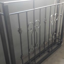 Metalek Kamil Talkowski - Metalowa balustrada z dekoracyjnymi elementami w kształcie spirali i liści, spawana konstrukcja, surowe wykończenie, widoczne spawy, szary odcień metalu.