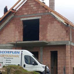 Darek Surgota - Budowa domu z czerwonej cegły, widoczni pracownicy na dachu podczas prac izolacyjnych. Na pierwszym planie samochód z reklamą ociepleń.