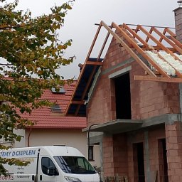 Darek Surgota - Budowa domu z ociepleniem pianką PUR na dachu, widoczna konstrukcja więźby i fragment ocieplenia. Na pierwszym planie firmowy bus z reklamą ociepleń.