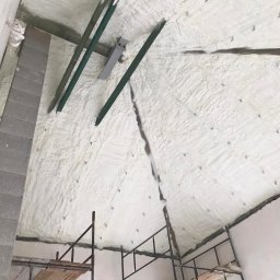 Darek Surgota - Poddasze po natrysku pianki PUR, widoczne metalowe profile i rusztowanie. Biała, nierówna powierzchnia izolacji z widocznymi punktami mocowania.