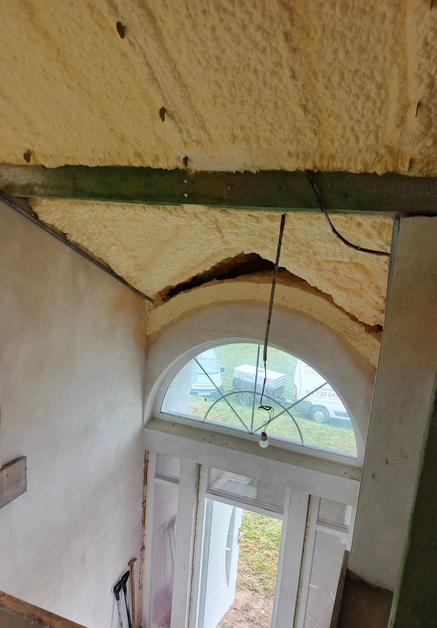 Poddasze z oknem łukowym w trakcie ocieplania pianką PUR, widoczne narzędzia i fragment elewacji. Charakterystyczna faktura pianki.