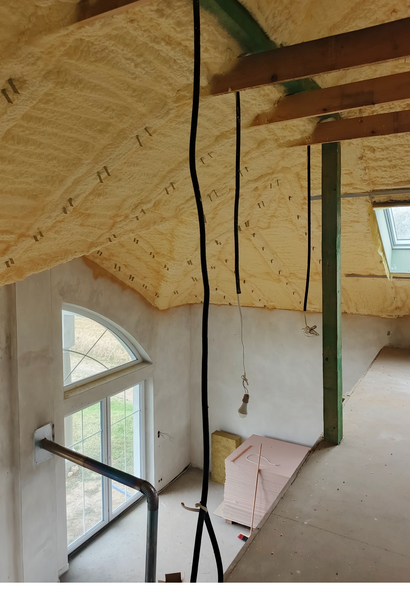 Poddasze ocieplone pianką PUR z widocznymi elementami konstrukcyjnymi, instalacją elektryczną i oknem dachowym. Widok z góry na ocieploną powierzchnię.